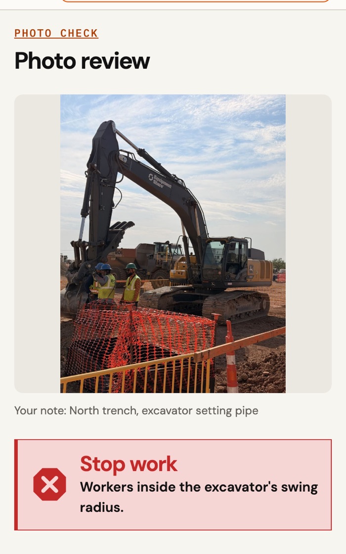 Photo Check flags a stop-work hazard: workers inside an excavator's swing radius